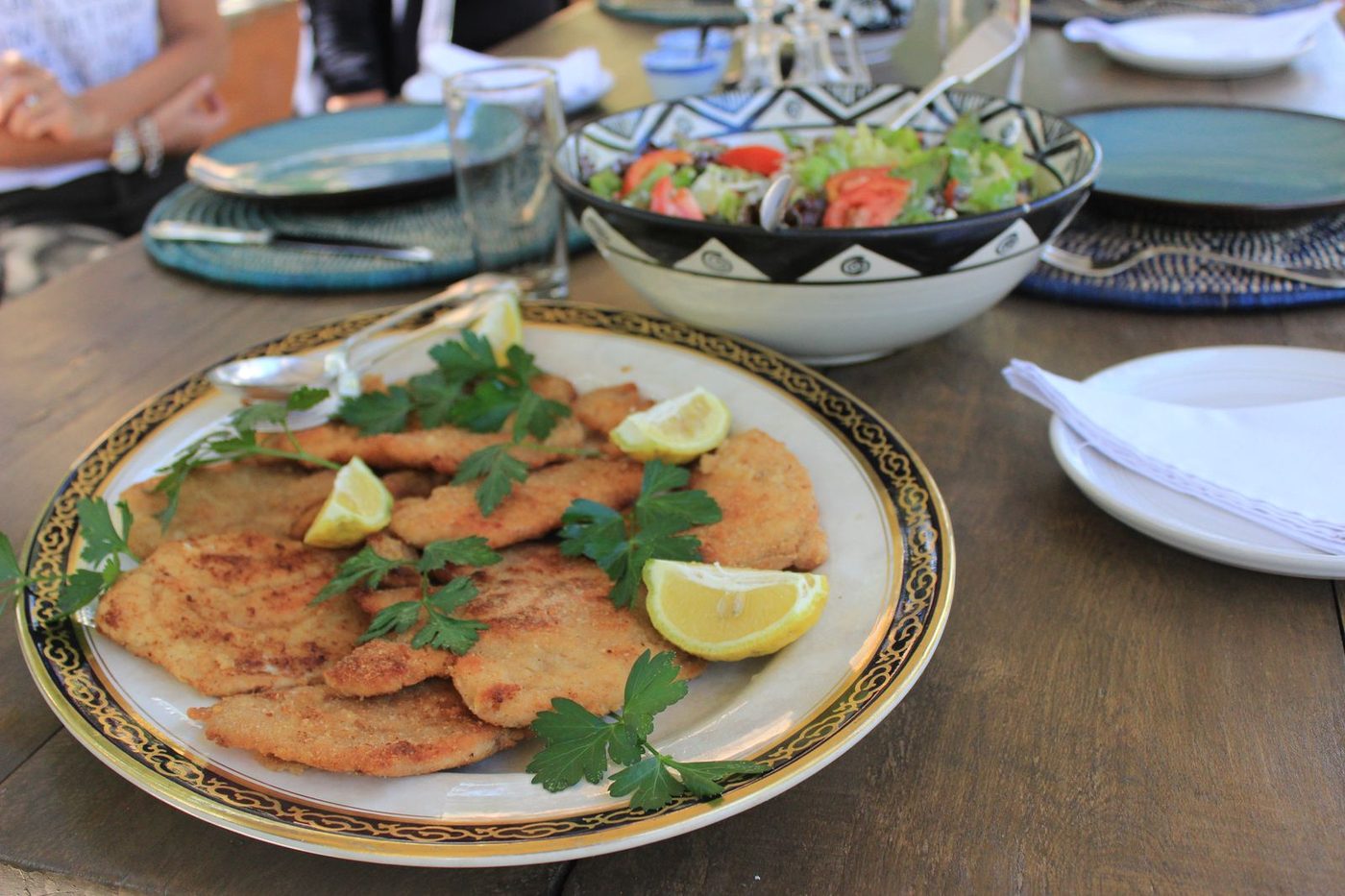 Cotoletta milanese on gold-rimmed plate with fresh salad in African patterned bowl