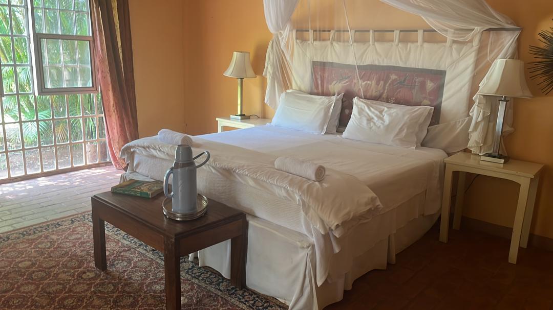 The Family Cottage — warm apricot walls, white linen bed with mosquito net canopy, French doors opening to tropical garden