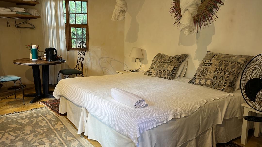 The Pool Cottage — whitewashed walls, African print cushions, woven mosquito net, tea station, and kilim rug