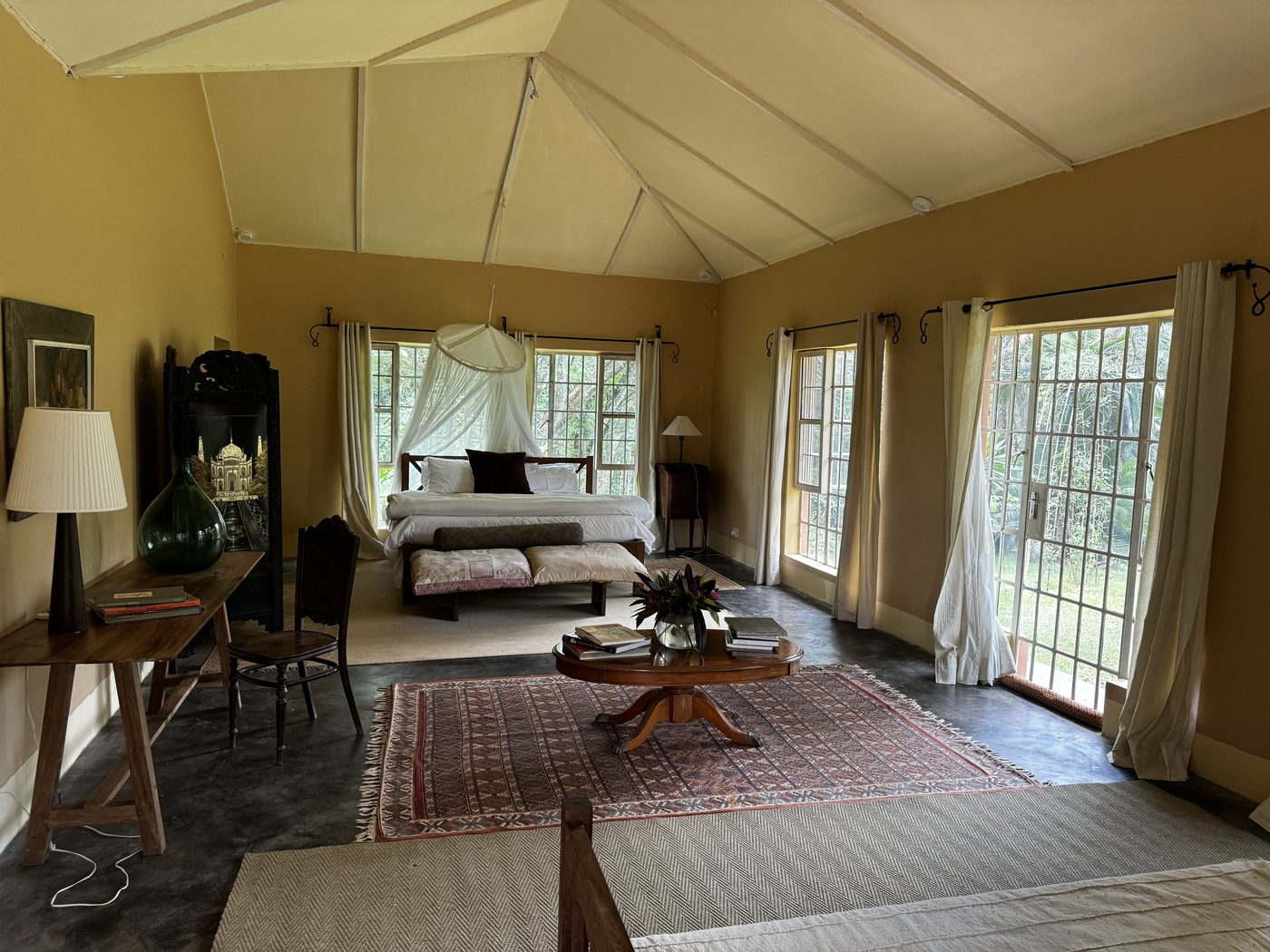 Pool Cottage — ochre walls, vaulted ceiling, dark polished floors, bed with mosquito net