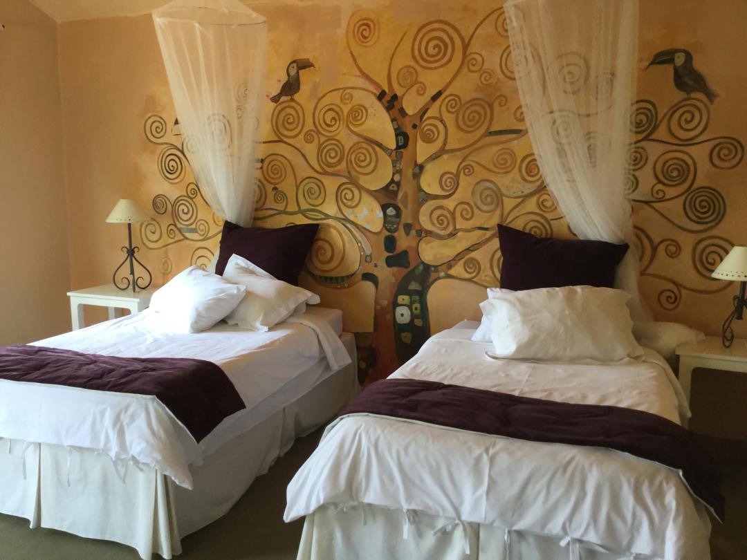 The Tree of Life Room — twin beds with Klimt-inspired mural, golden spirals, toucans, and deep purple throws